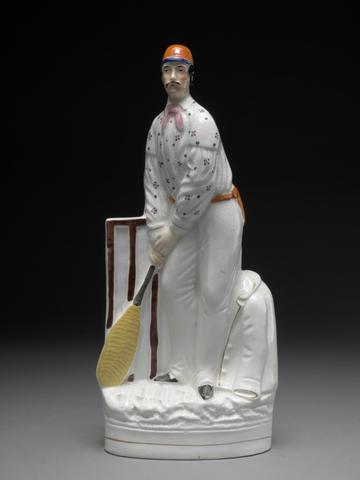 Staffordshire pottery Cricketers - a pair: each in iron-red cap, spotted shirt and red sash, one bowling, one batting