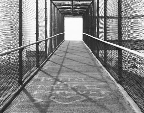 Robert Adams, Untitled (fenced-in walkway with graffiti), 1970–74