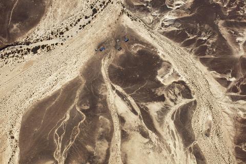 Fazal Sheikh, LATITUDE: 30°27'41"N / LONGITUDE: 34°58'40"E, November 14, 2011. Bedouin encampment beside a seasonal stream in the Aravah desert mountains leading to the Ramon Crater. In this arid zone, Bedouin herders search for areas near seasonal waterways in order to tap into the yearly rainfall, which allows for the growth of vegetation for their herds to graze. The geological alluvium is a loose, unconsolidated soil or sediment that has been eroded, reshaped by water, and re-deposited in a non-marine setting. The larger particles of sand and gravel here are comprised largely of flint., from the series Desert Bloom, 2011